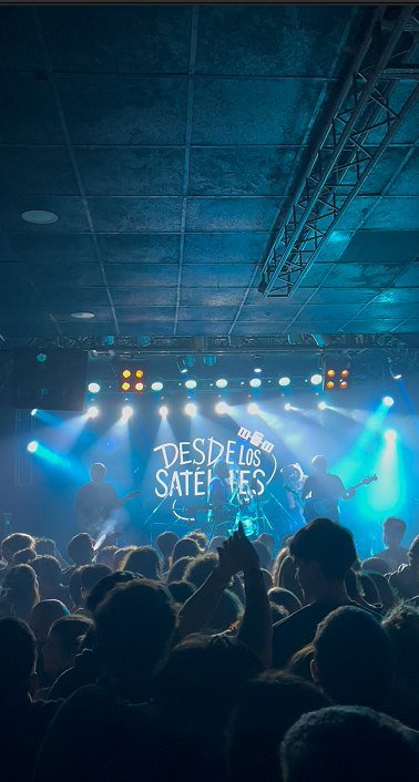 La banda en el escenario con el logo proyectado y el público adelante